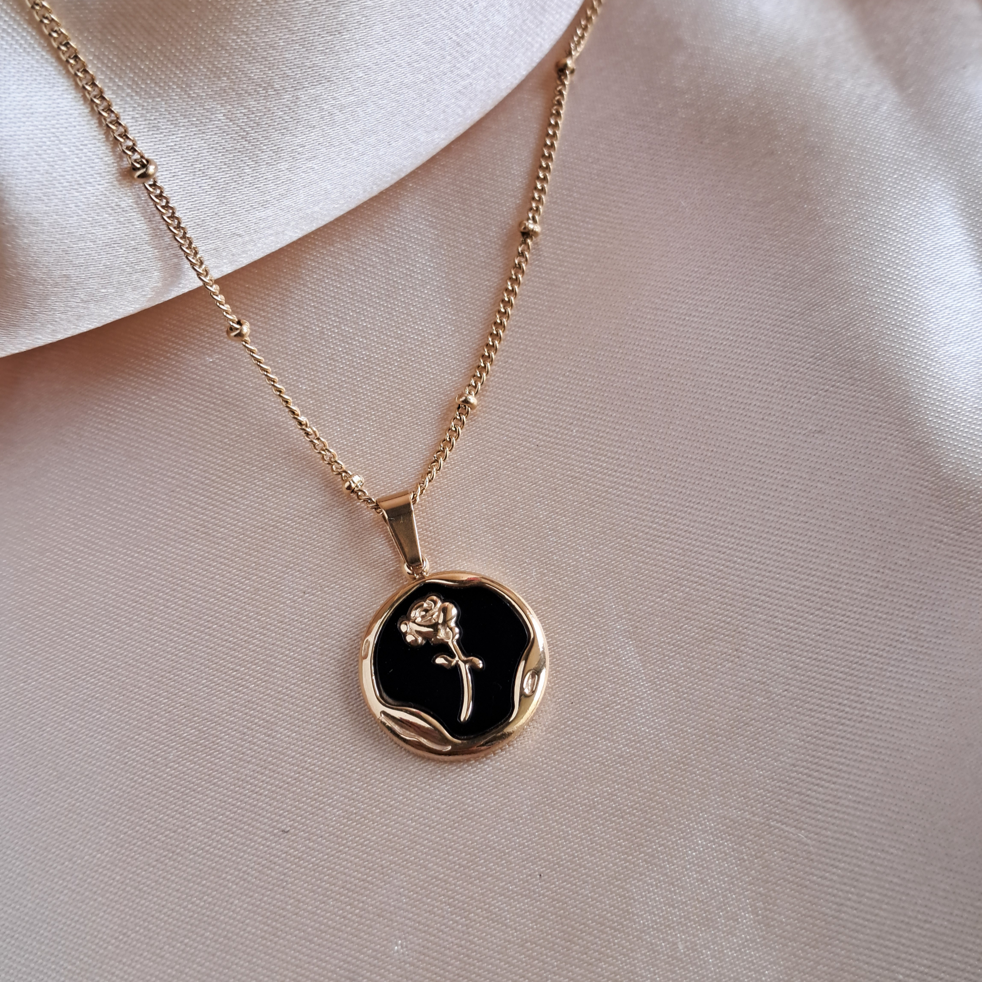 Golden rose necklace with round pendant on black background