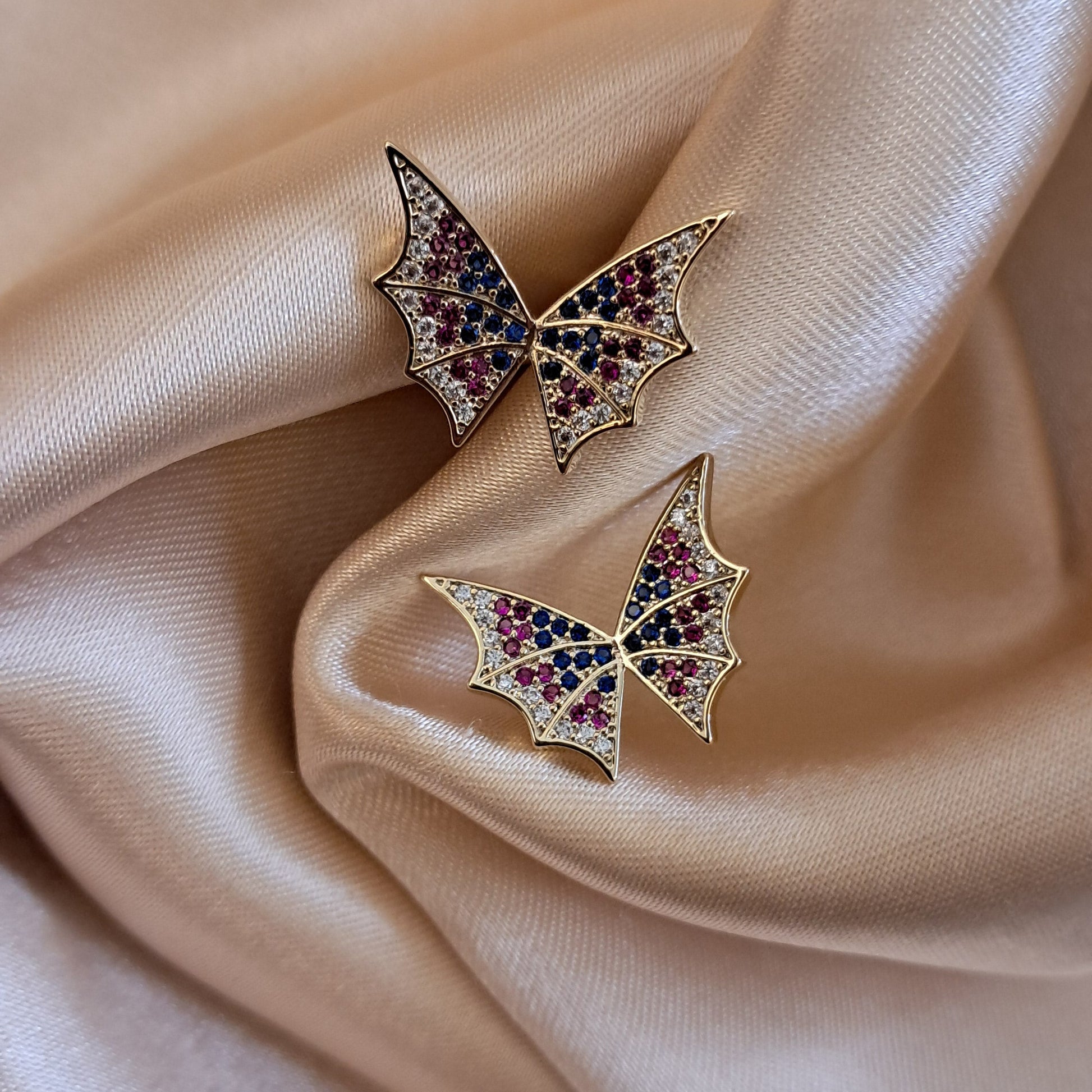 Pair of butterfly-shaped earrings with gemstones on a beige fabric background