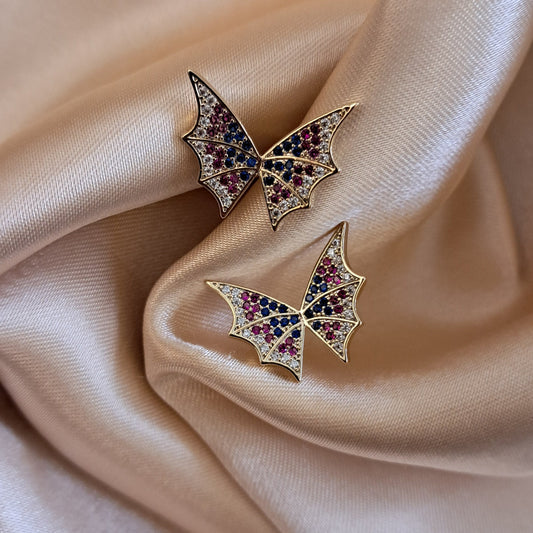 Pair of butterfly-shaped earrings with gemstones on a beige fabric background
